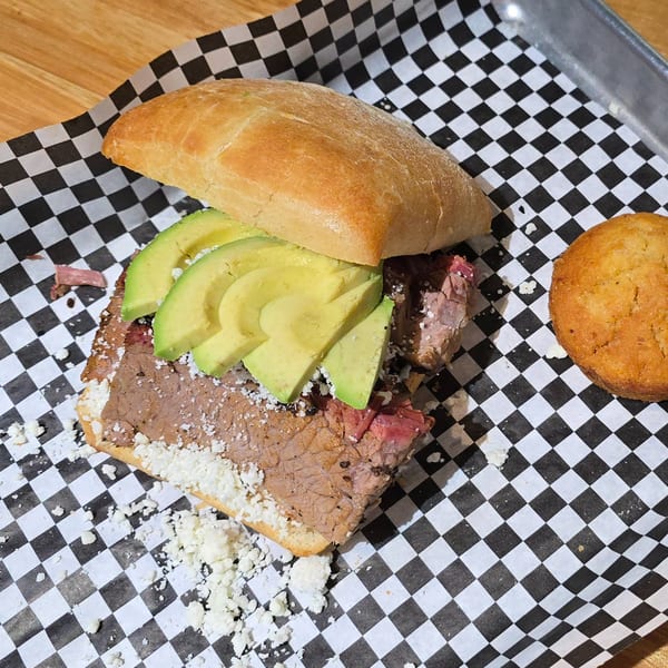 Holy Smokes BBQ brisket sandwich with avocado and cheese, served with a cornbread muffin.