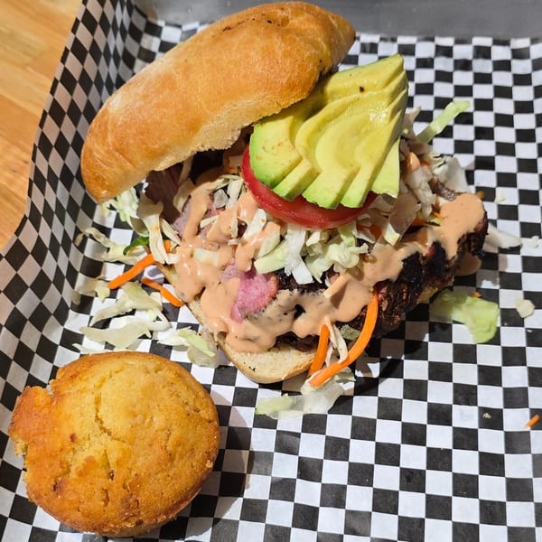 Holy Smokes BBQ sandwich with avocado, tomato, and sauce, served with a cornbread muffin.