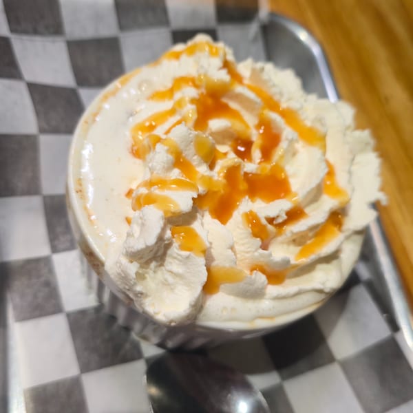 A white mug of coffee topped with whipped cream and caramel drizzle on a checkered paper.
