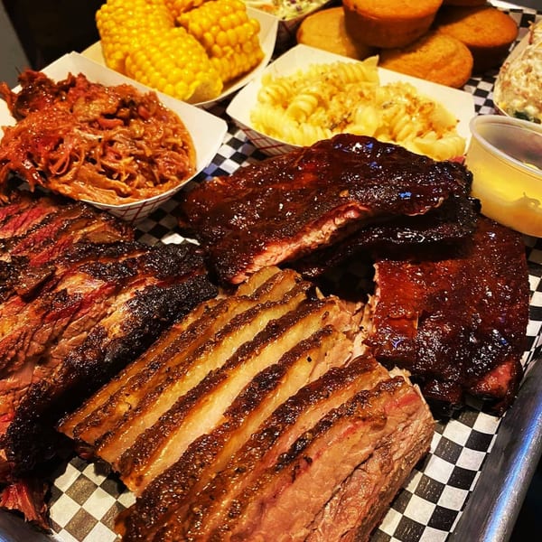 A Holy Smokes BBQ platter with ribs, brisket, pulled pork, corn, mac and cheese, and cornbread.
