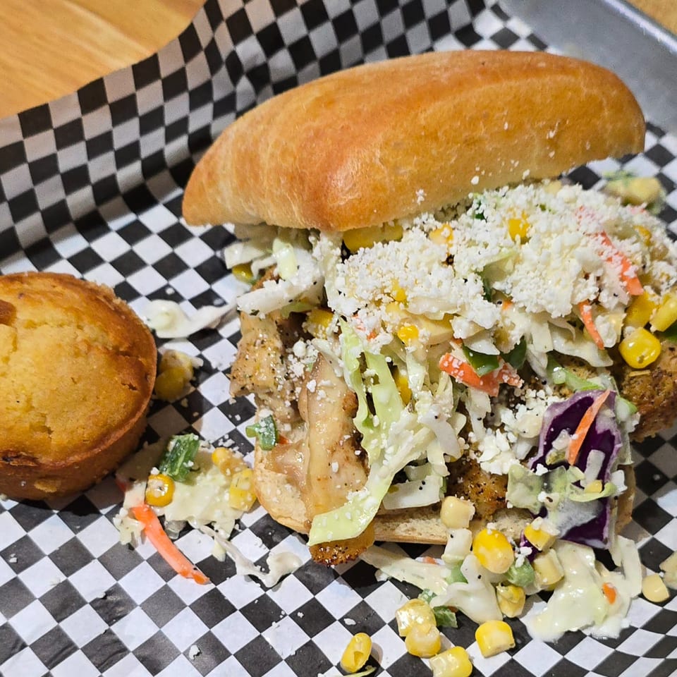 Holy Smokes BBQ sandwich with coleslaw, corn, and cheese, served with a cornbread muffin.